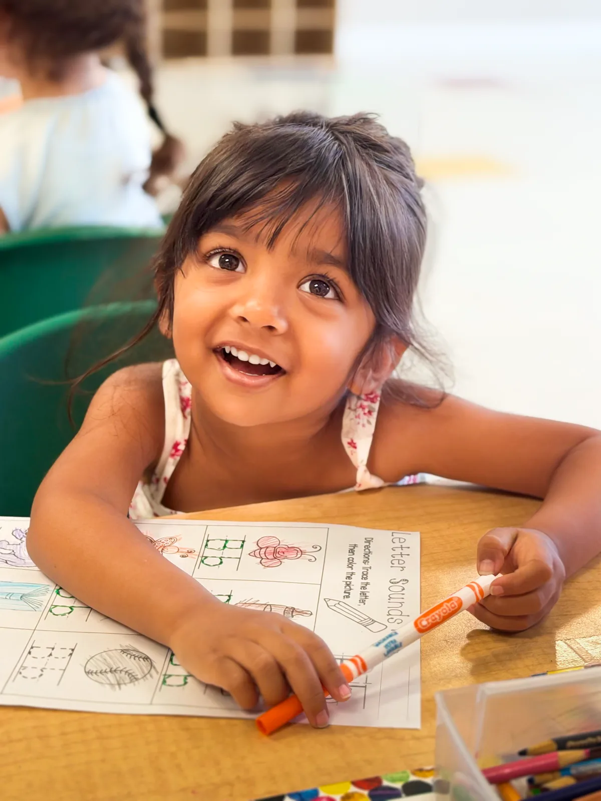A Starbright student looking up with a bright smile while tracing letters on a letter sounds worksheet